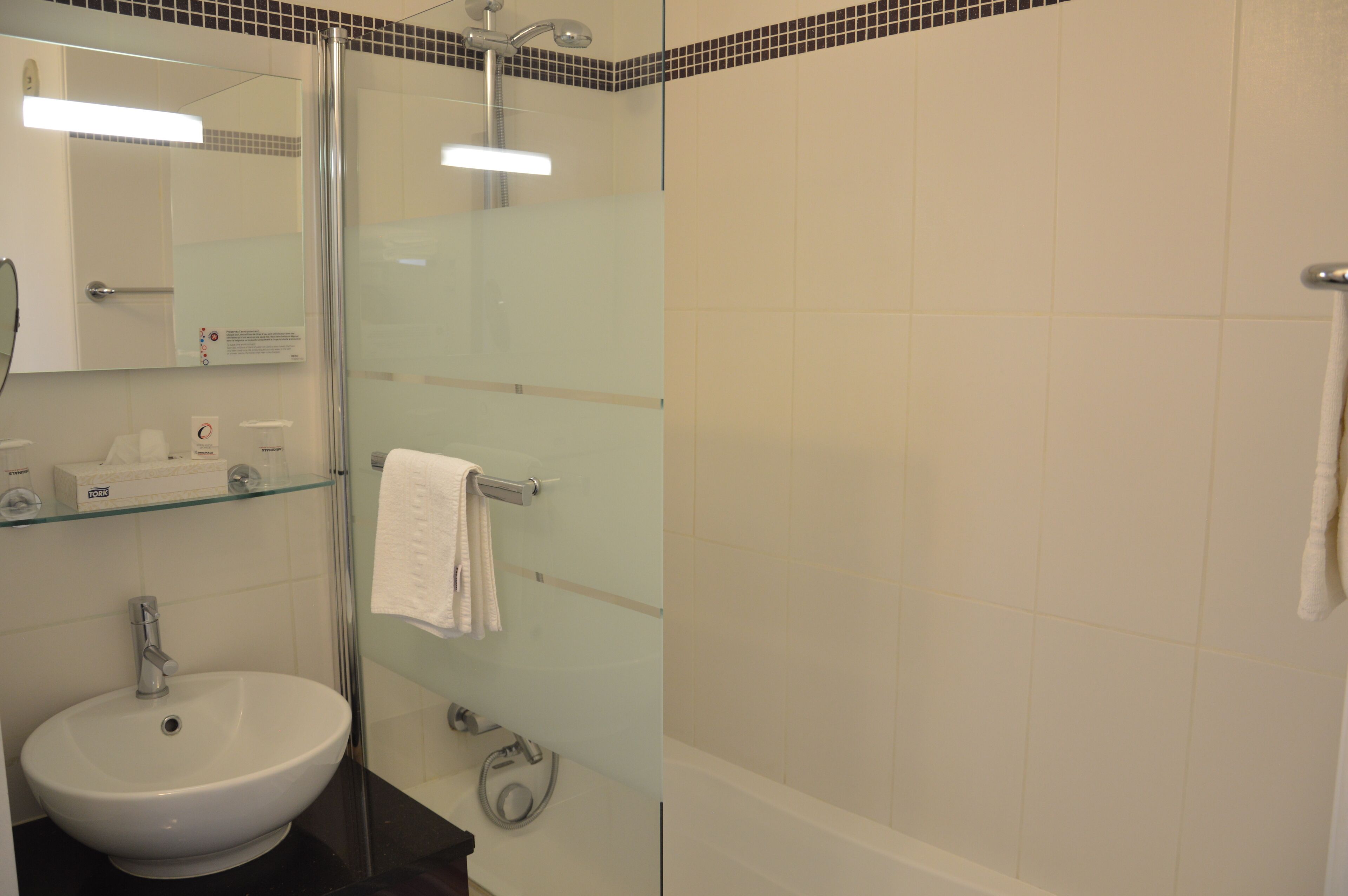 Ein Badezimmer mit einer Duschkabine aus Glas, einem weißen Waschbecken und einer Glasablage für Pflegeartikel.