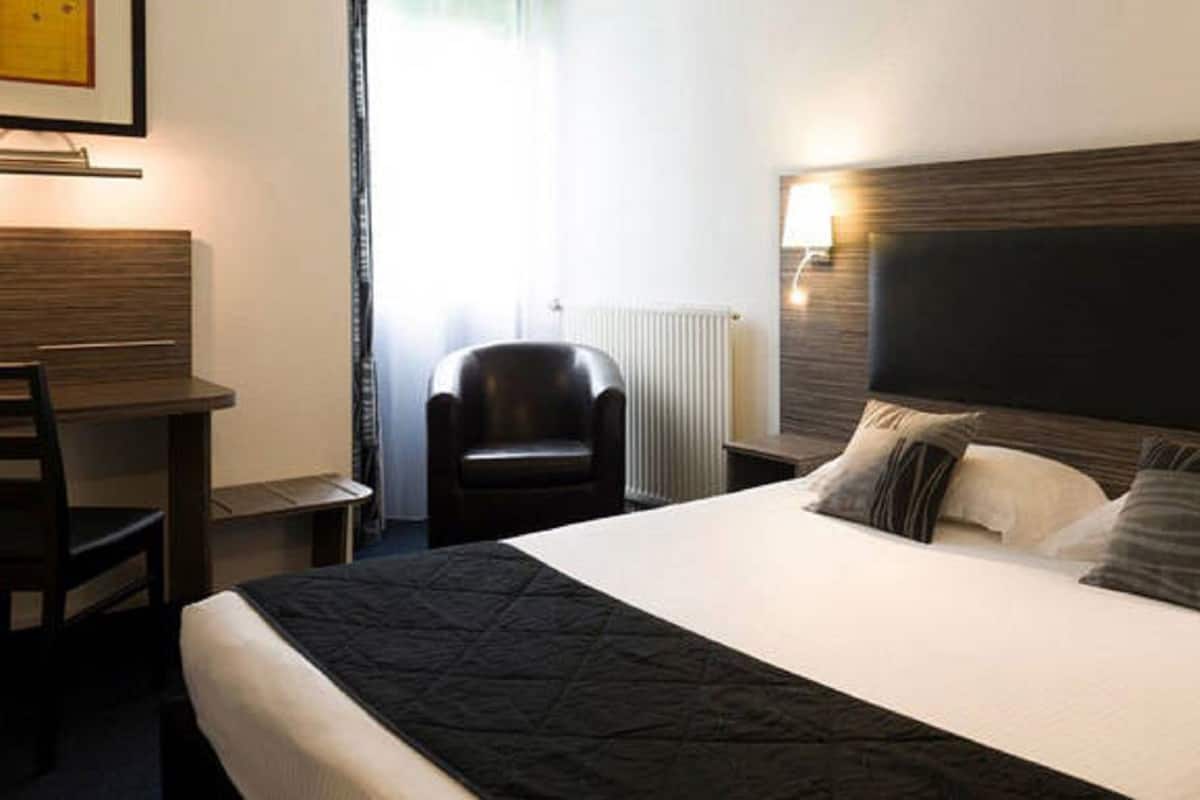 A hotel room with a large bed, a desk, a chair, and a radiator.