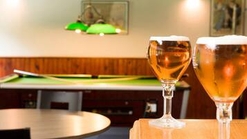 Due bicchieri di birra su un tavolo di legno in una stanza con tavolo da biliardo e boiserie.