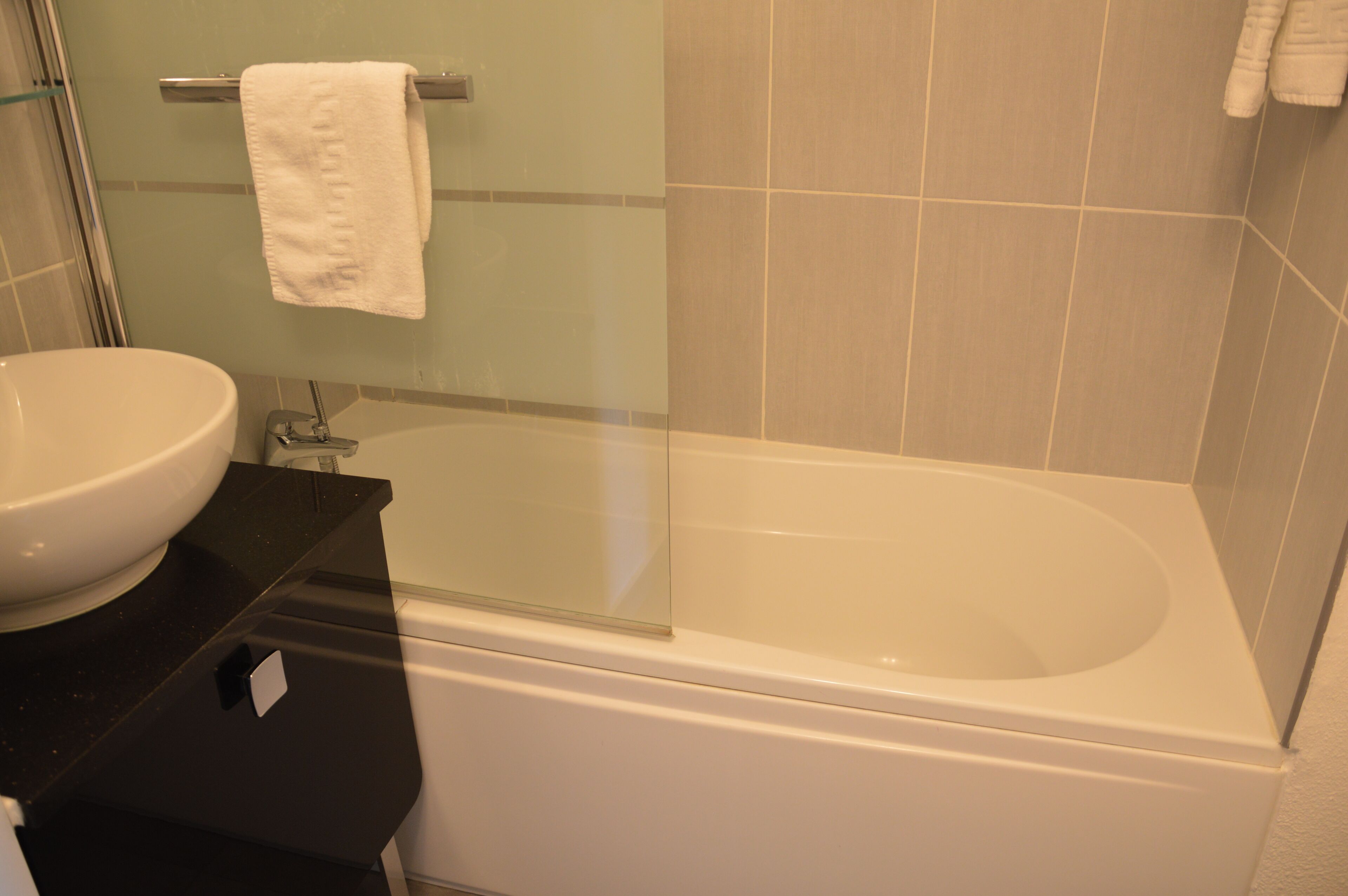 Een badkamer met een witte wastafel, een glazen douchebad en een handdoek aan een metalen rek.