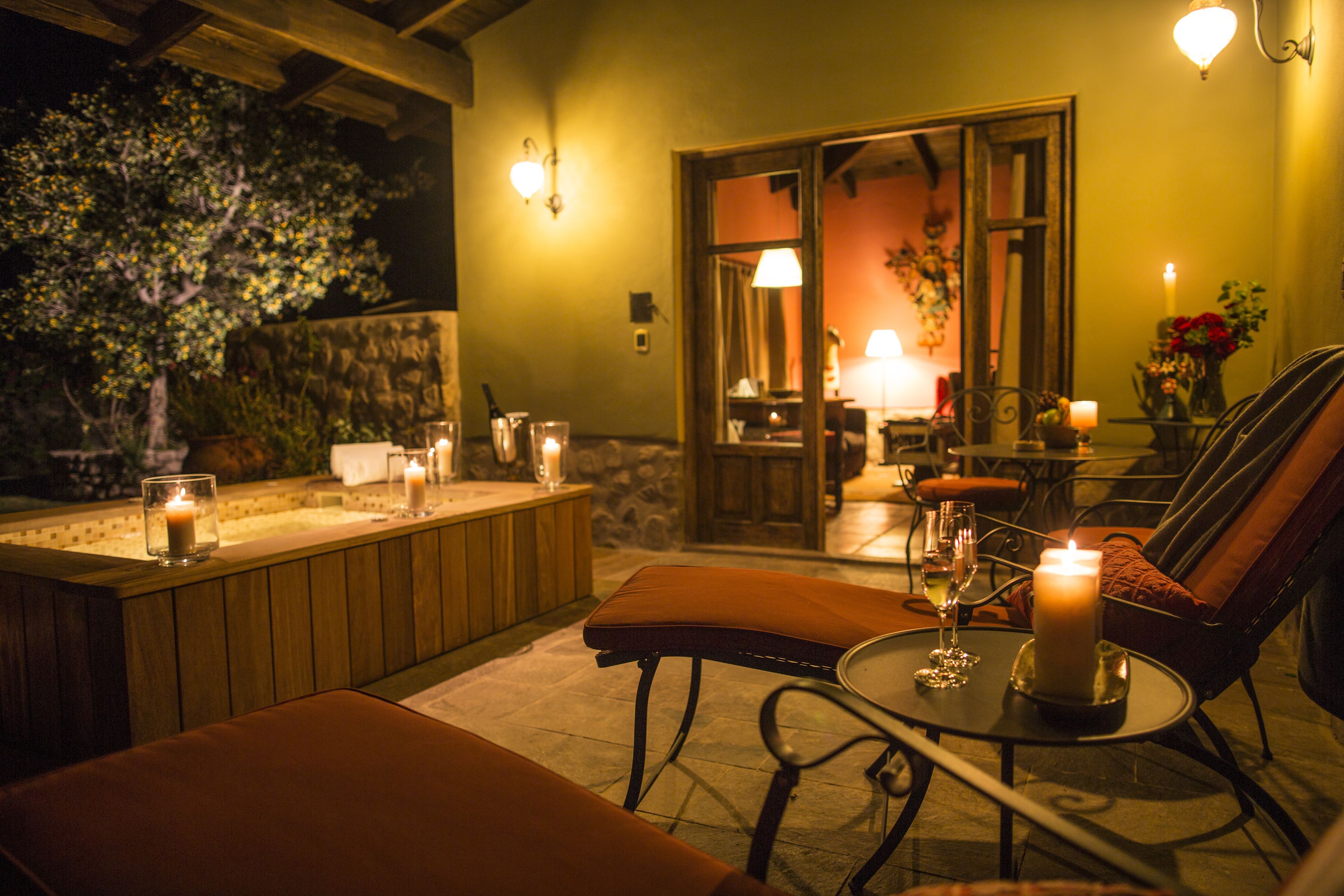 A cozy outdoor seating area with a cushioned bench, a table with a candle, and a glass of wine.