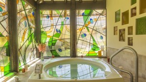 Un cuarto de spa con una bañera grande, vidrieras de colores y un panel de control en la pared.