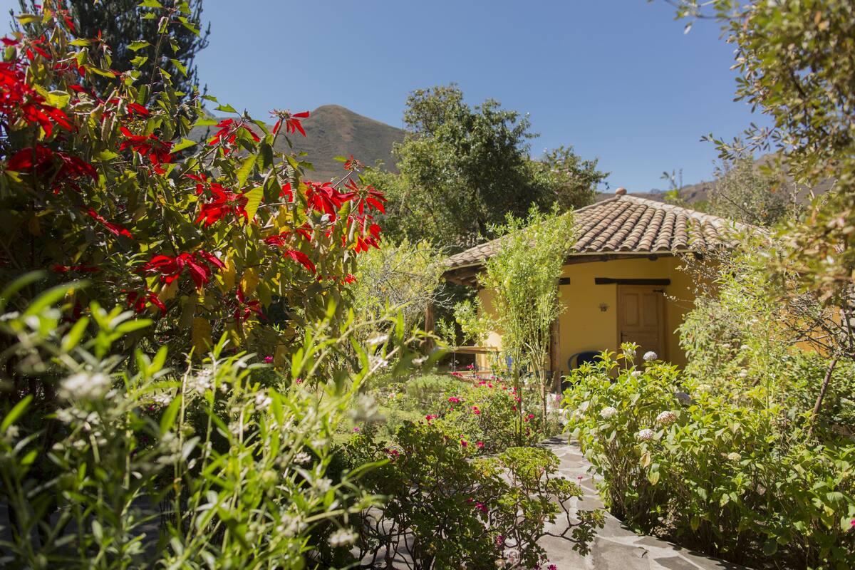 A yellow building with a tiled roof, surrounded by lush greenery and red flowers.
