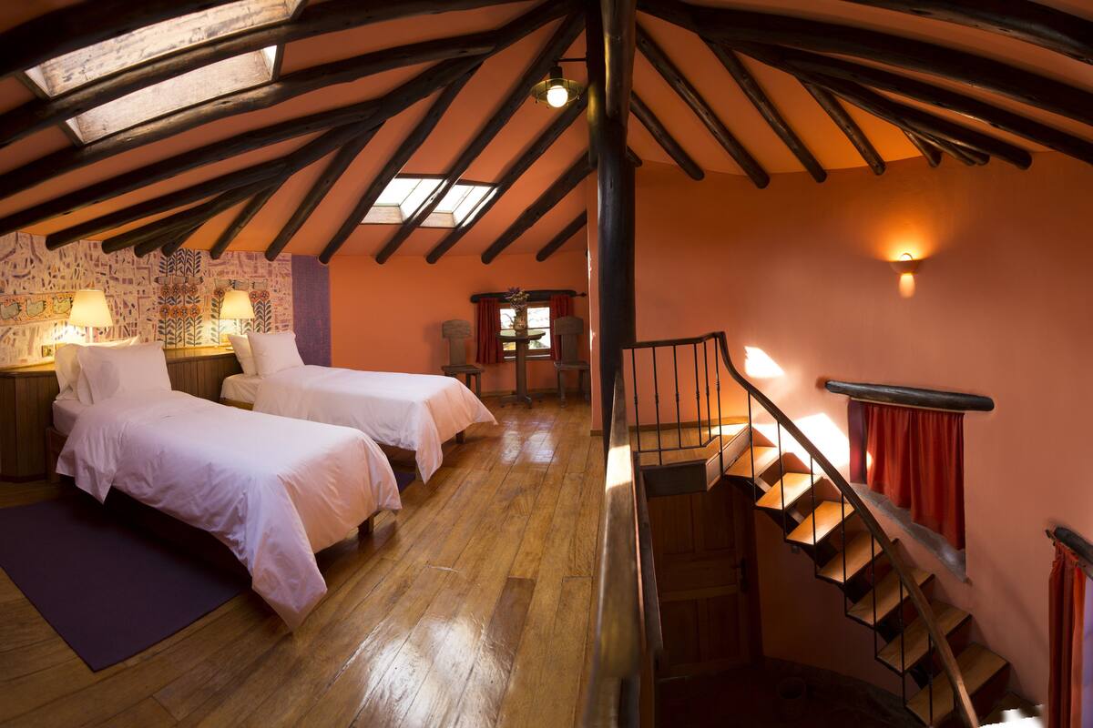 A room with two beds, wooden flooring, a staircase, and a sloped ceiling with skylights.