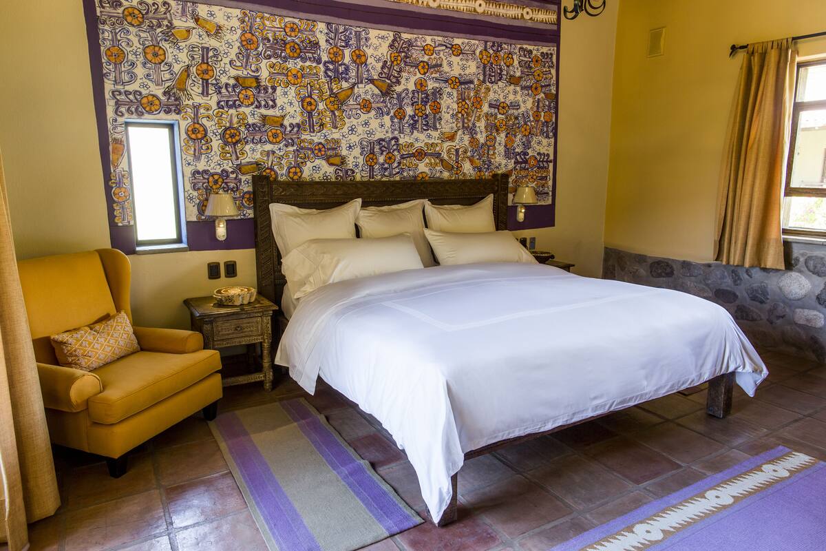 A bedroom with a large bed, a chair, a nightstand, and a decorative wall.