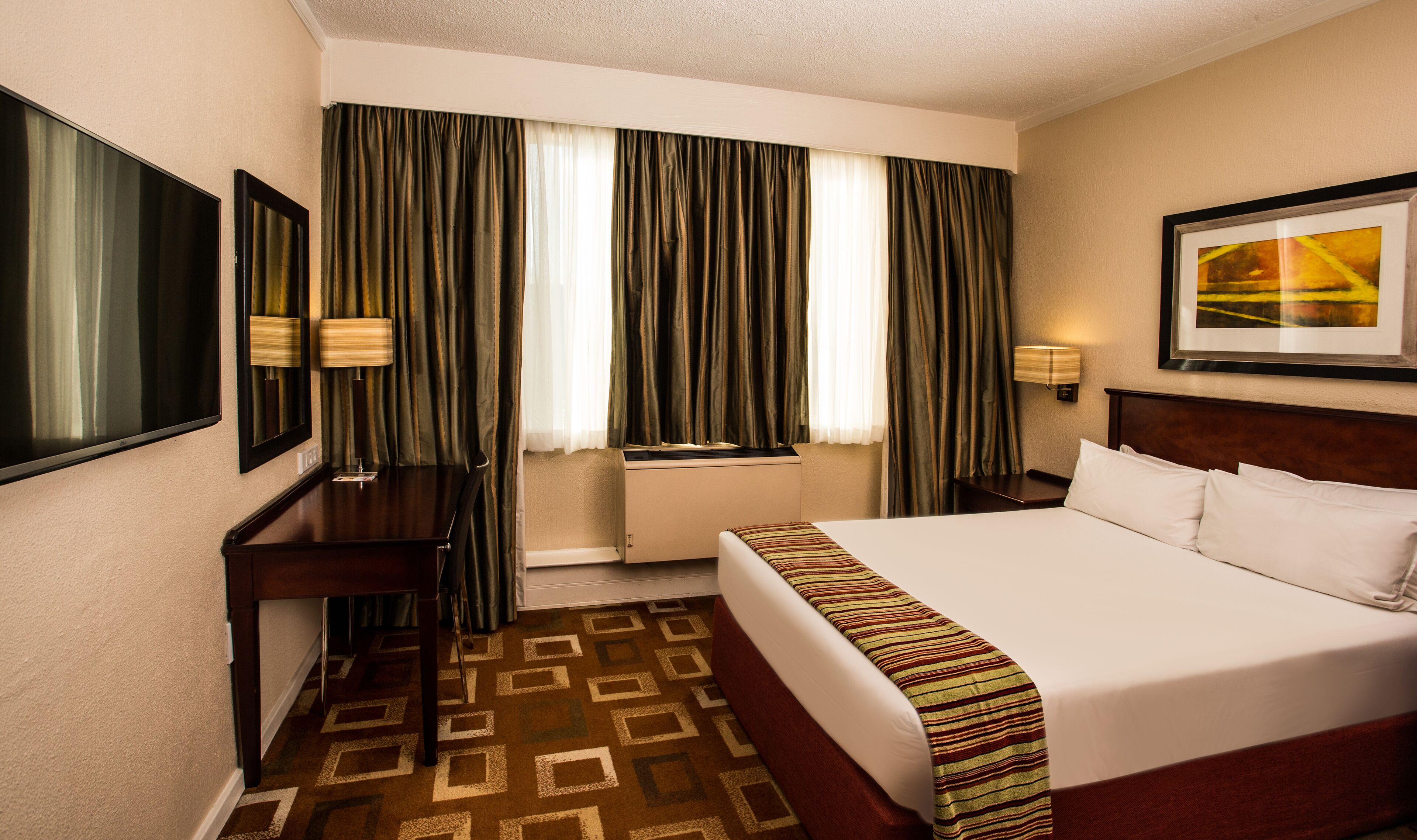 Habitación de hotel con una cama grande, un escritorio, una silla, un televisor y una ventana con cortinas.
