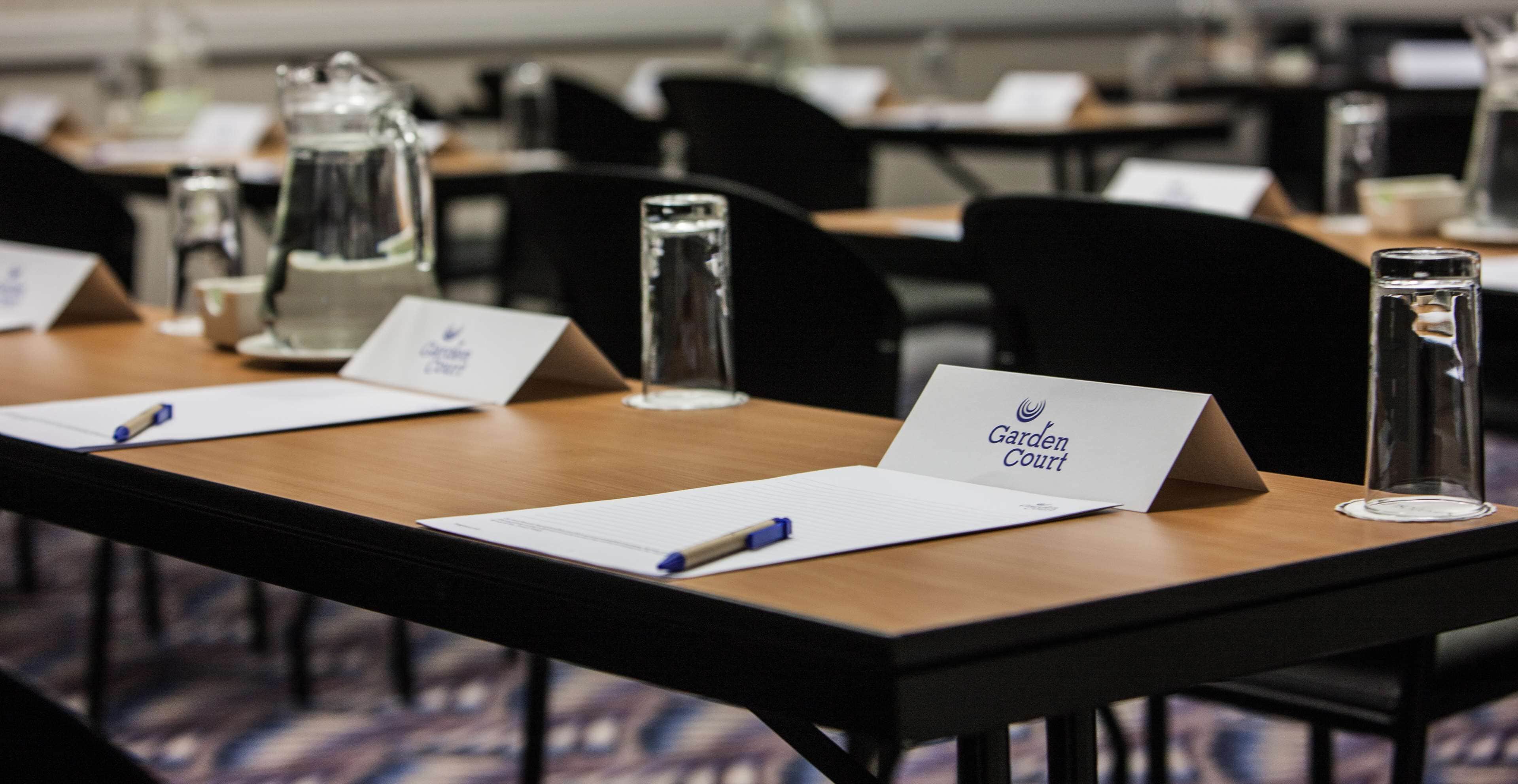 Un salón de conferencias con mesas equipadas con tarjetas de identificación, bolígrafos y botellas de agua de vidrio.