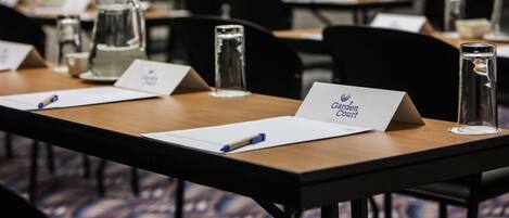 Un salón de conferencias con mesas equipadas con tarjetas de identificación, bolígrafos y botellas de agua de vidrio.
