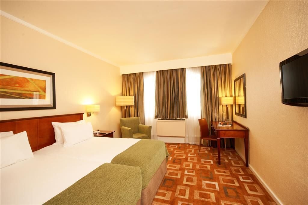 Une chambre d’hôtel avec un grand lit, deux fauteuils, un bureau, une télévision et une moquette à motifs.