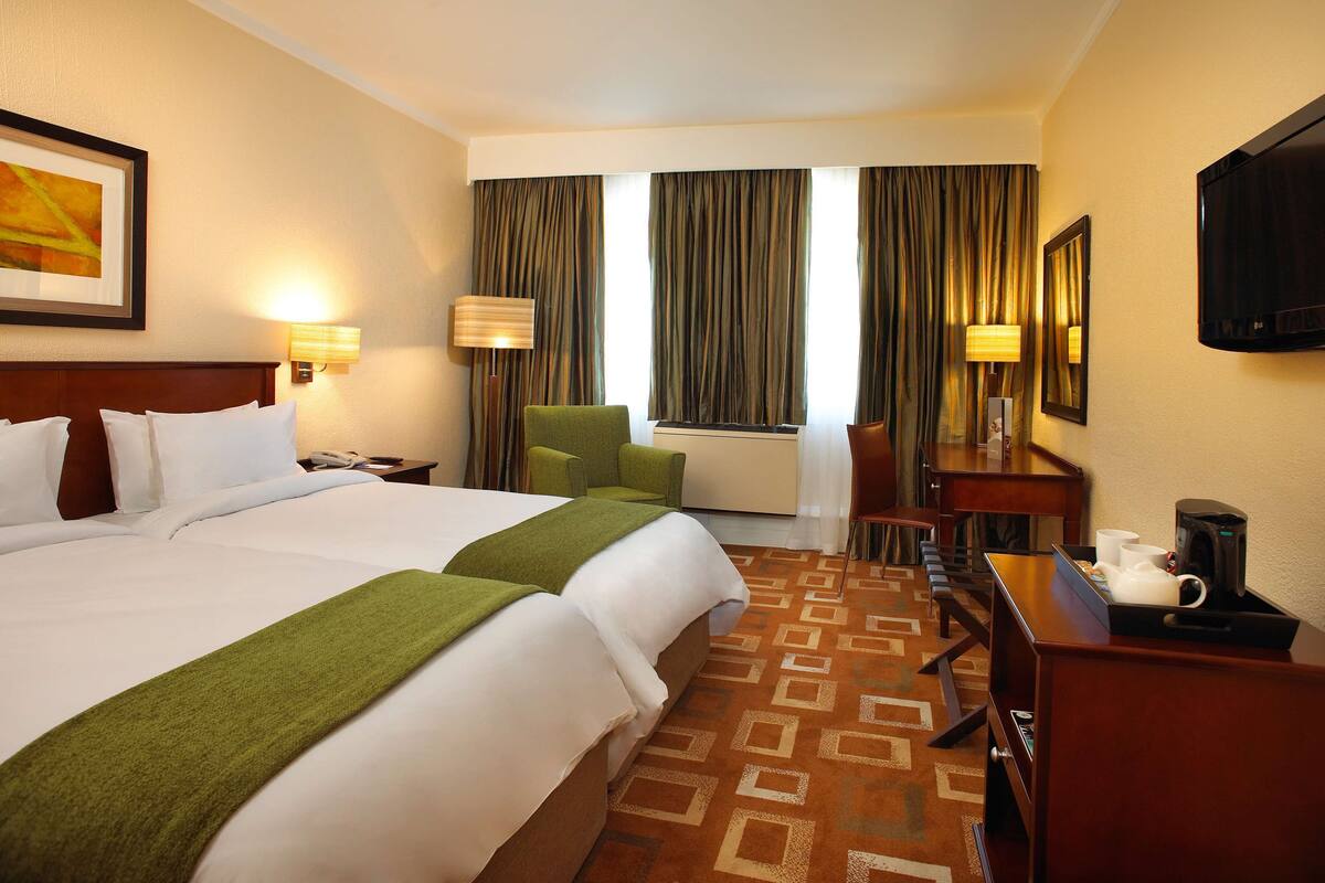 Quarto de hotel com uma cama grande, uma escrivaninha com cafeteira e uma televisão na parede.