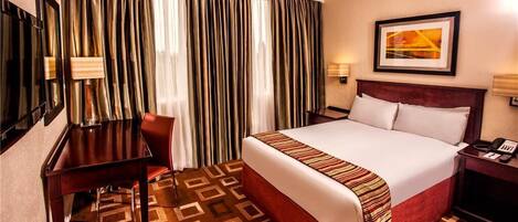 A hotel room with a large bed, a desk, a chair, a telephone, and a painting on the wall.