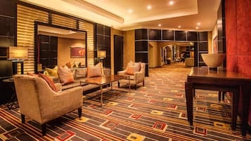 Un moderno vestíbulo de hotel con un sofá, sillones, una mesa de centro y una alfombra estampada.
