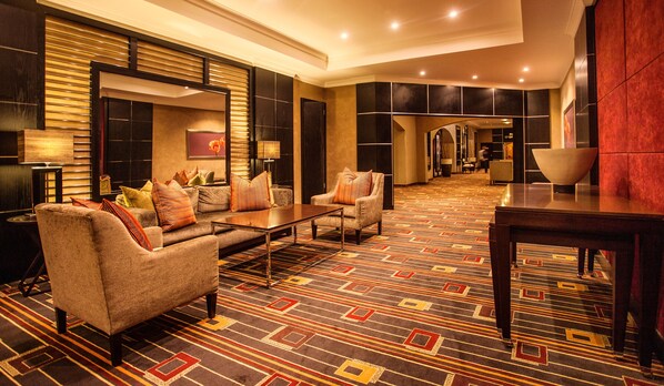 Un moderno vestíbulo de hotel con un sofá, sillones, una mesa de centro y una alfombra estampada.