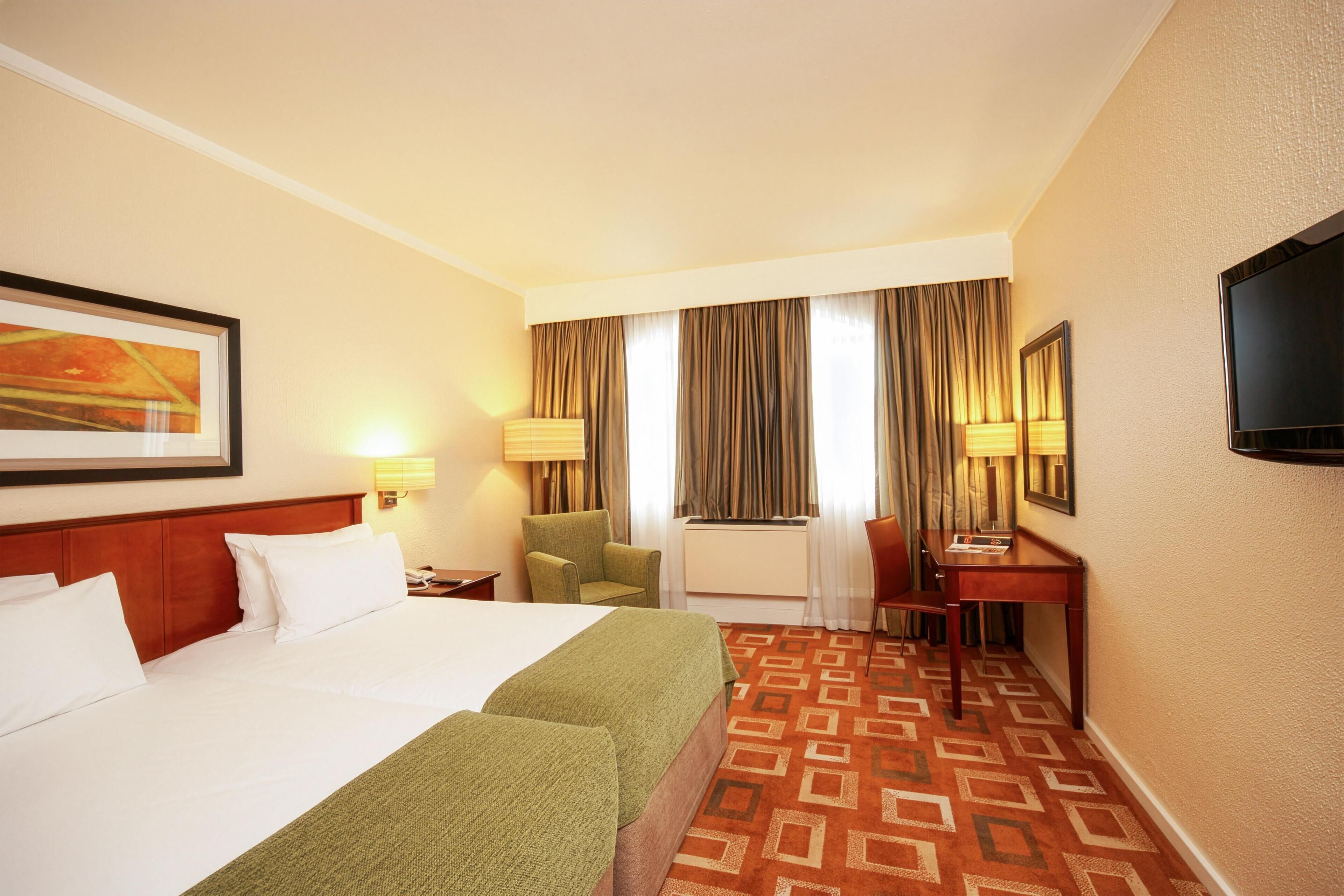 A hotel room with a large bed, a desk, a chair, and a television.