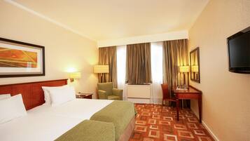 A hotel room with a large bed, a desk, a chair, and a television.
