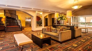 A hotel lobby with a sofa, coffee table, and a staircase. - Garden Court O.R. Tambo International Airport (Kempton Park)