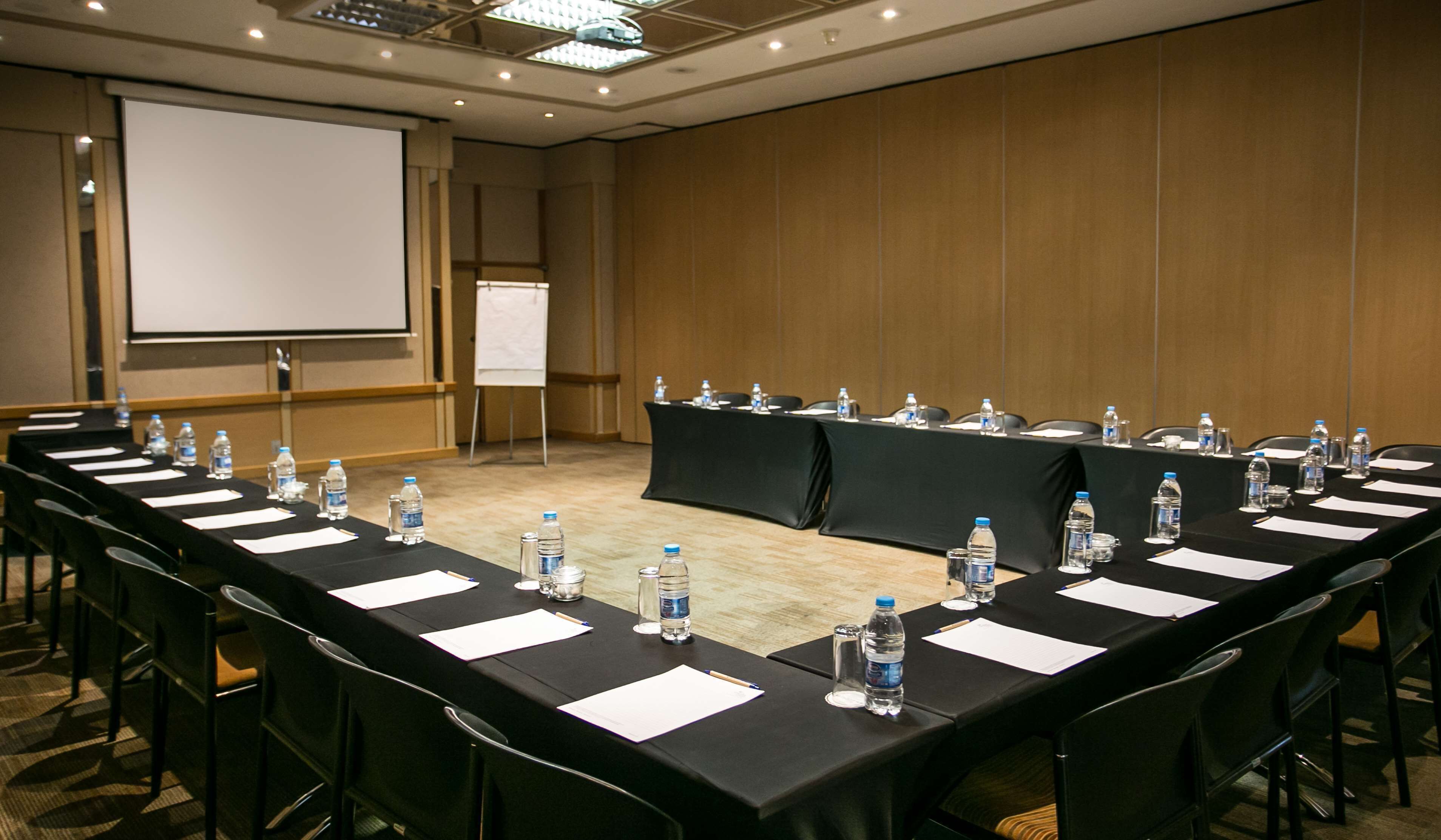 Une salle de conférence dotée d’une longue table préparée pour les réunions, avec des bouteilles d’eau, du papier et des chaises.