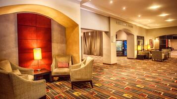 A hotel lobby with a patterned carpet, seating area with armchairs, a conference center sign, and a reception desk.