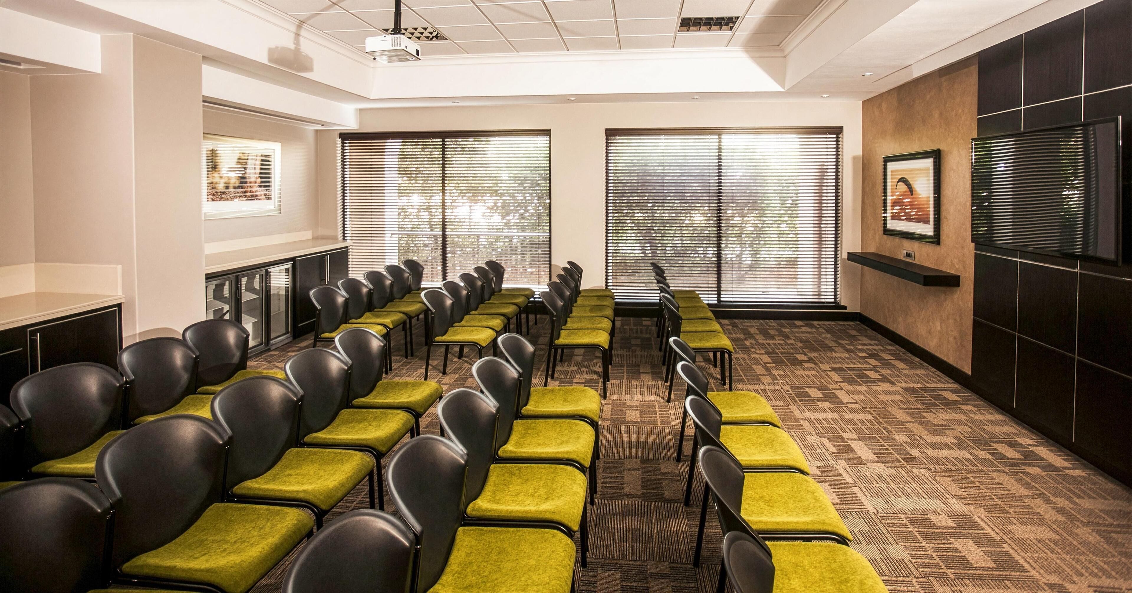 A conference room with rows of chairs, large windows, a projector, and a television.