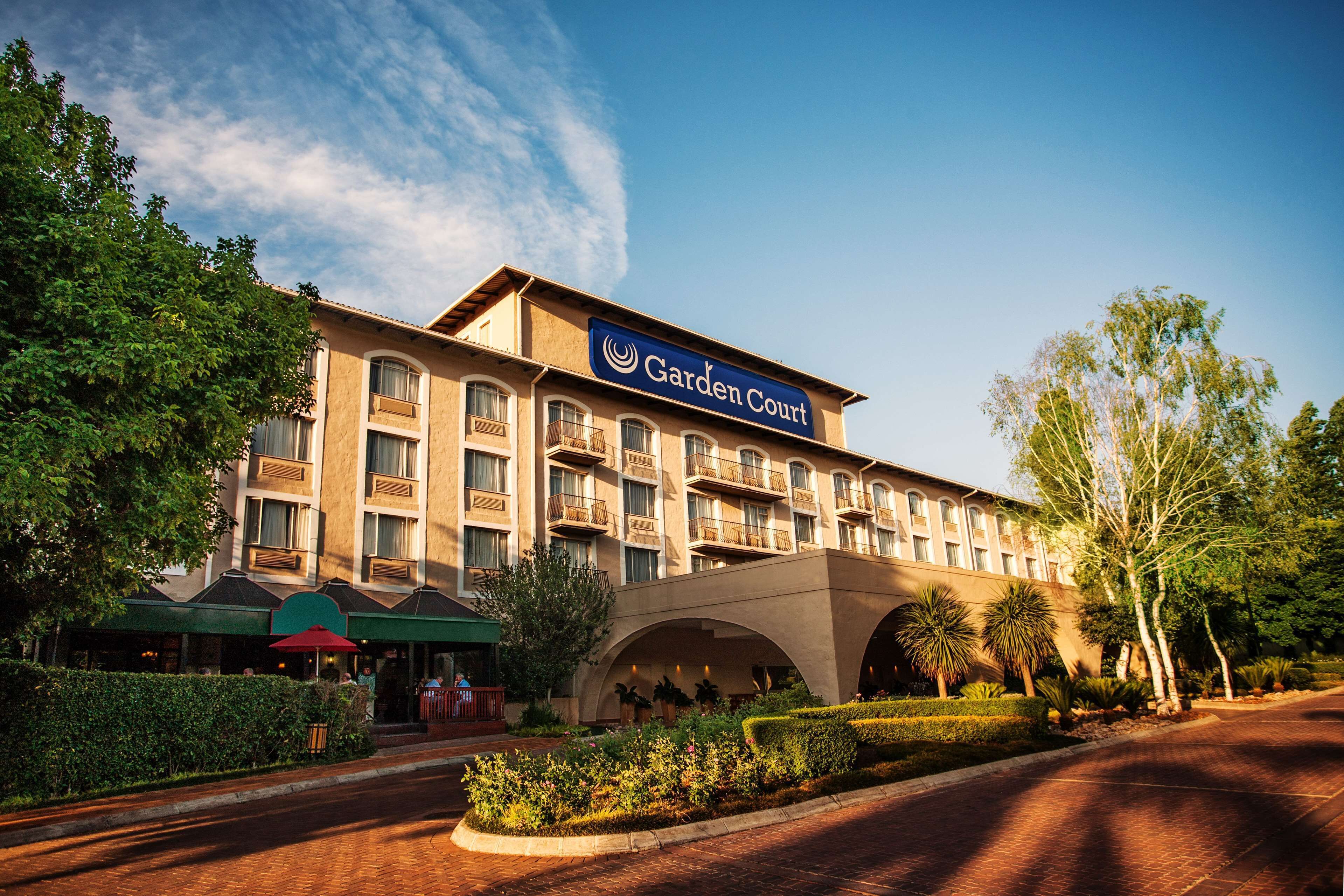 Un hotel con un llamativo letrero que dice "Garden Court", que cuenta con un patio central con plantas y zonas de estar.