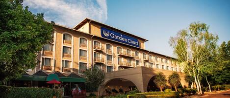 Un hotel con un llamativo letrero que dice "Garden Court", que cuenta con un patio central con plantas y zonas de estar.