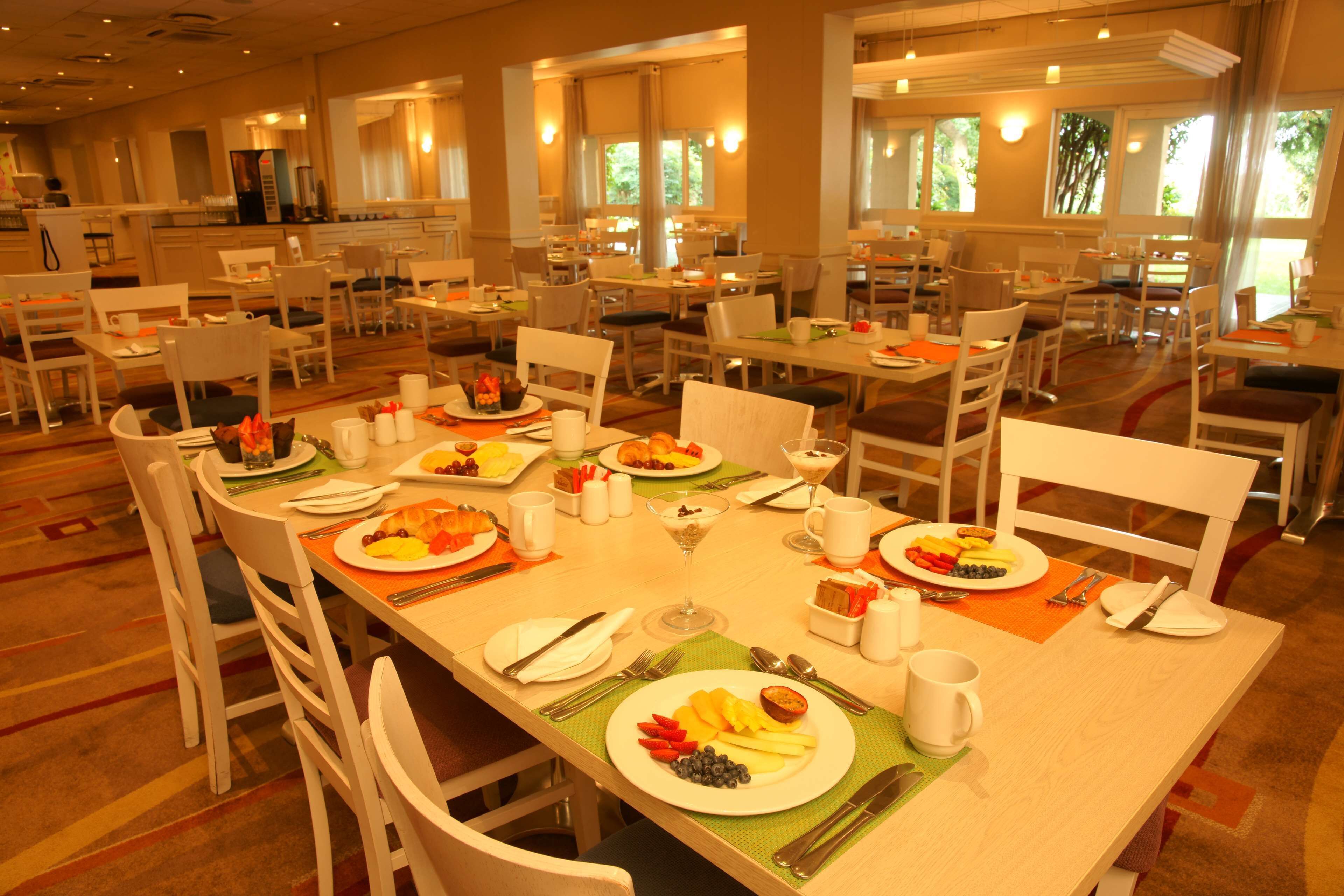 A spacious dining area with multiple tables and chairs, each set with plates of food, cutlery, and glasses.