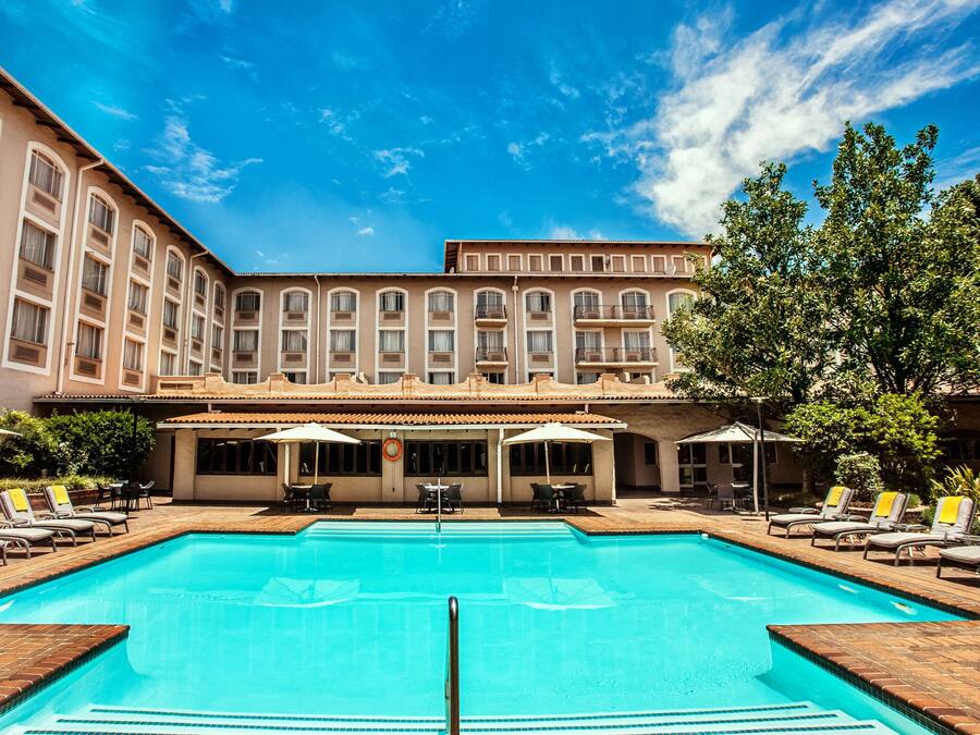 A pool area with lounge chairs and umbrellas, surrounded by a building with multiple windows and balconies.