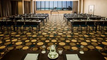 A conference room with a view of the beach, arranged tables with chairs, and a patterned carpet.
