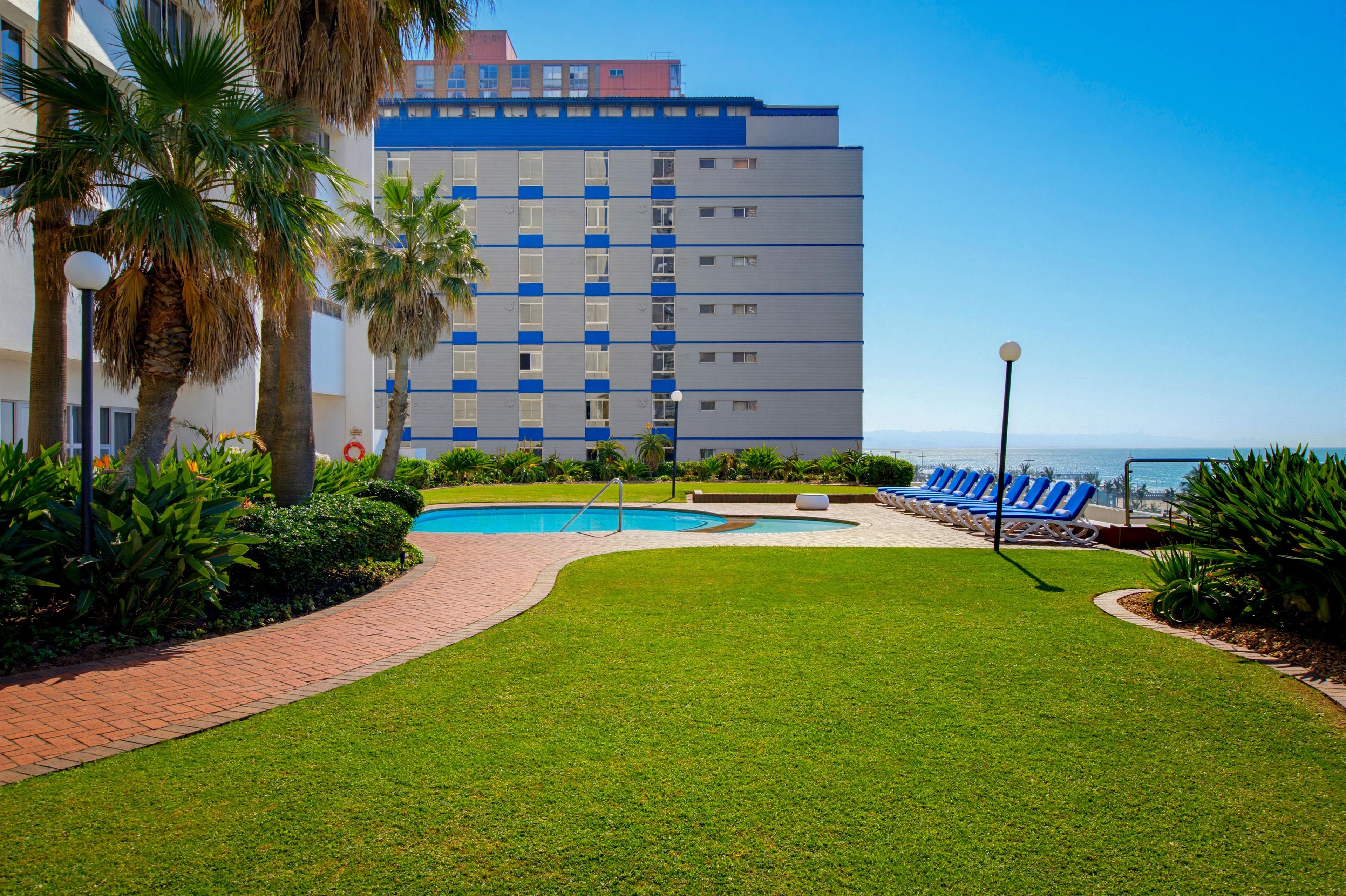 A hotel with a swimming pool, palm trees, and a view of the ocean.