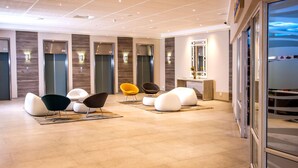 Een moderne lobby met een centrale zithoek, liften en een receptiebalie.