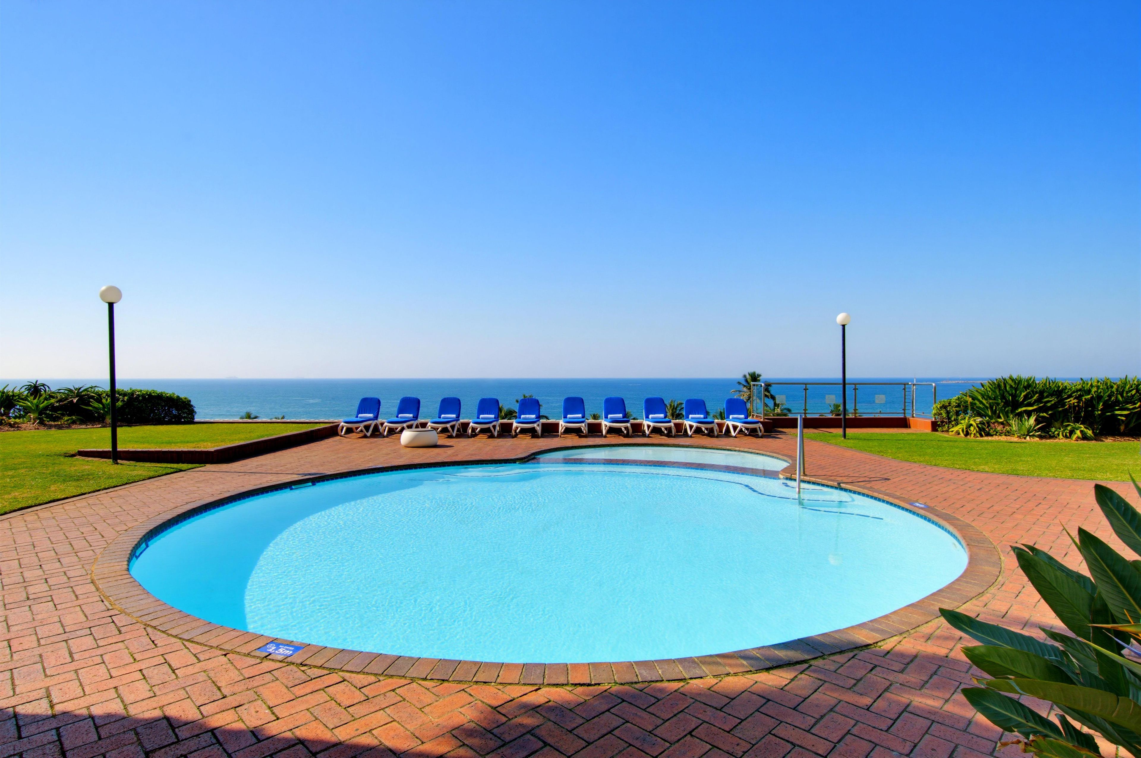A swimming pool with blue chairs and a view of the ocean.