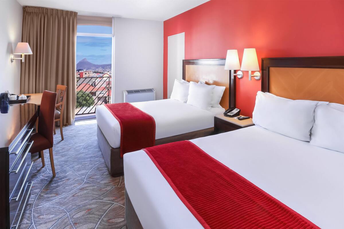 Une chambre d’hôtel avec deux lits, un bureau, une chaise et une vue sur la ville.