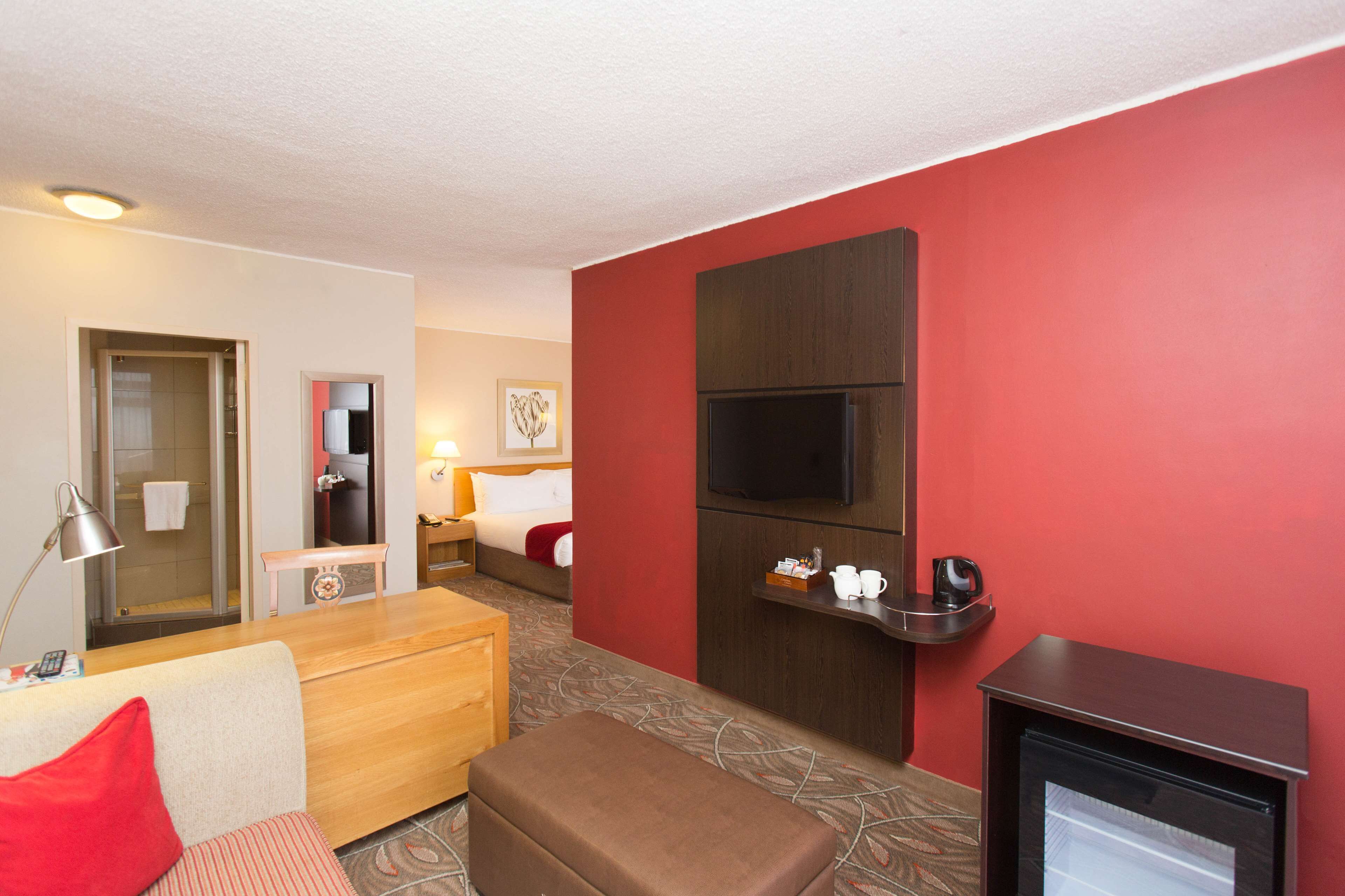 Une chambre d’hôtel avec un lit, un banc en bois, une petite table, une télévision et un réfrigérateur.