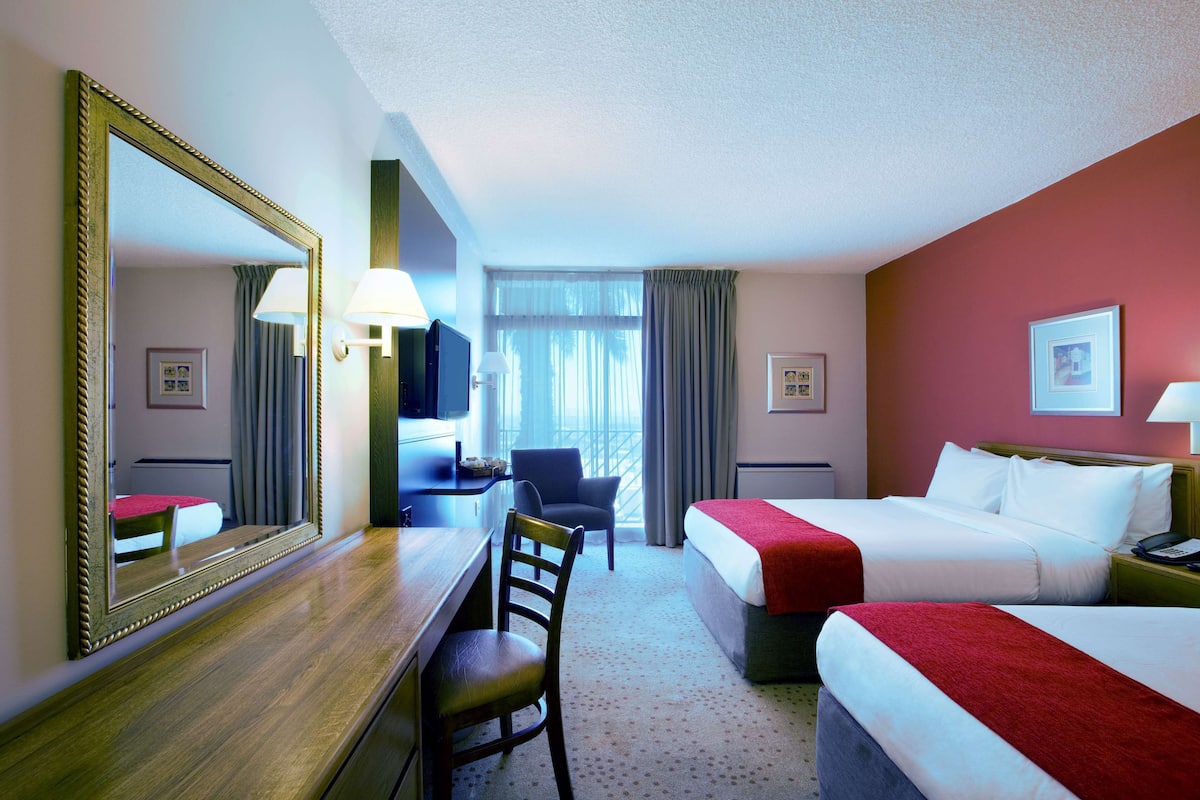 Une chambre d’hôtel avec deux lits, un bureau, une chaise, une télévision et une fenêtre avec des rideaux.