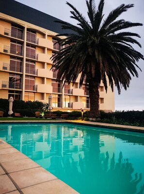 A hotel with a swimming pool, palm trees, and a building with balconies.