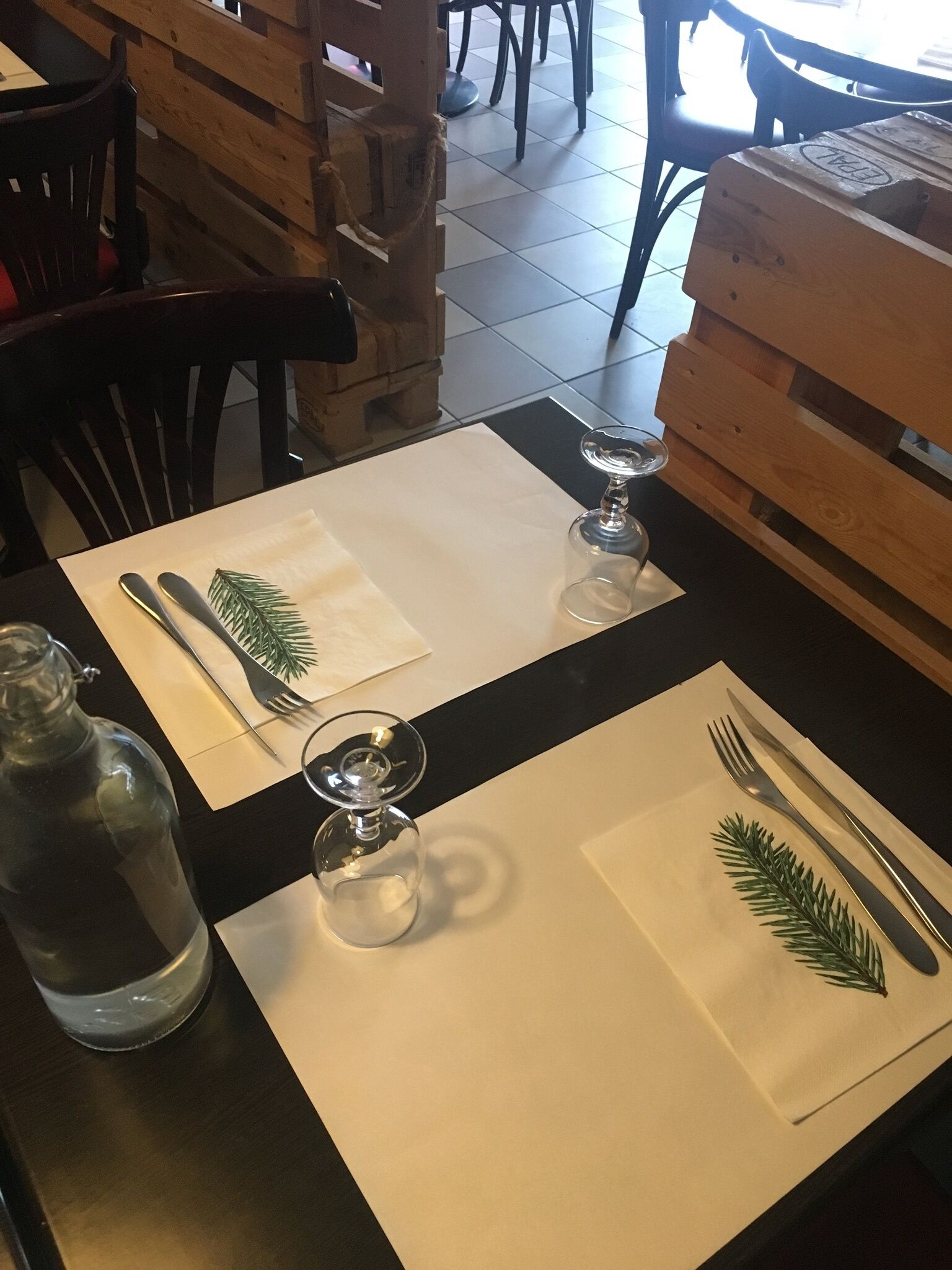 Une table à manger dressée avec une bouteille, deux verres à vin et des couverts sur des sets de table blancs.
