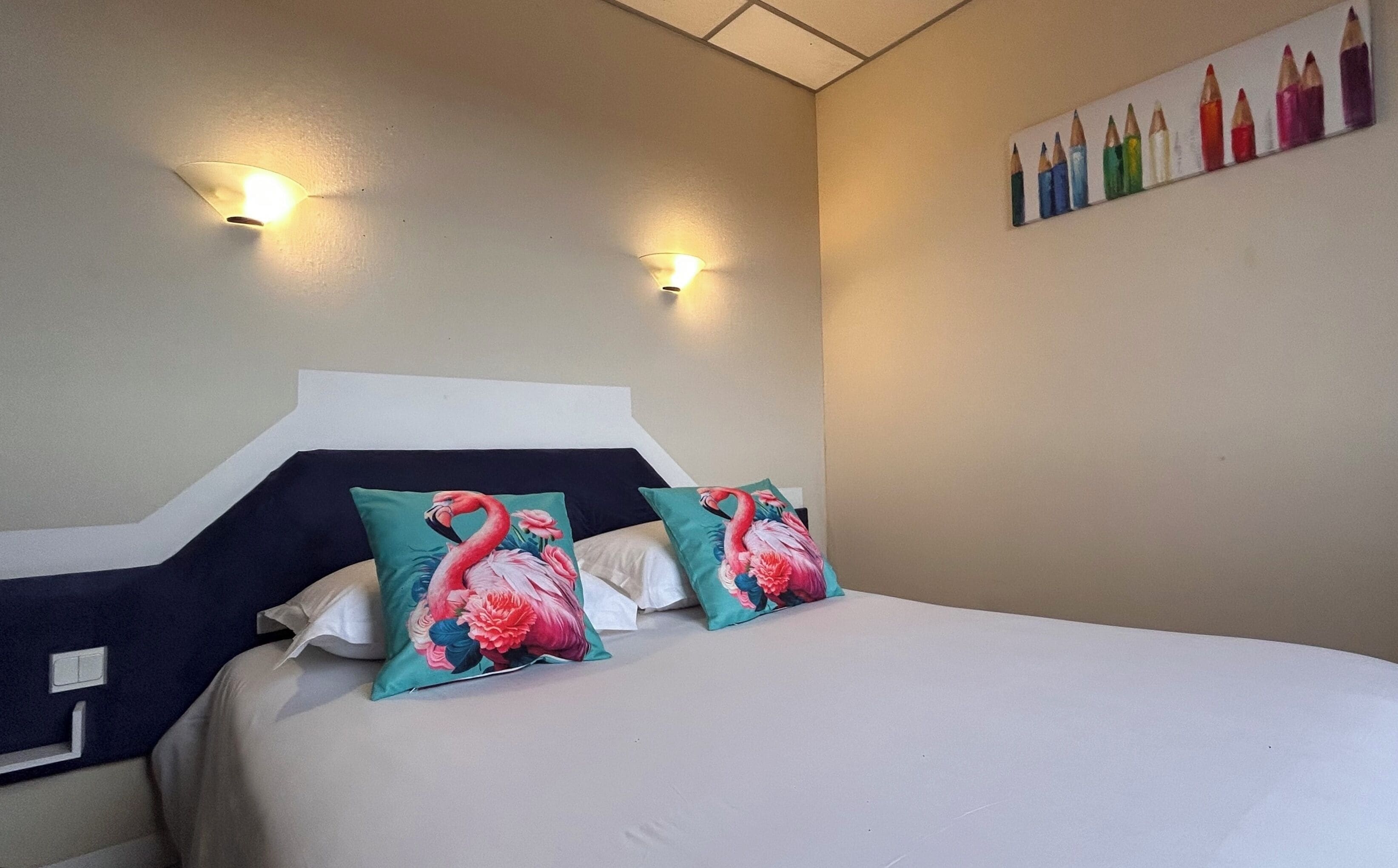 Habitación de hotel con una cama, dos luces fijadas a la pared y un cuadro de lápices de colores.