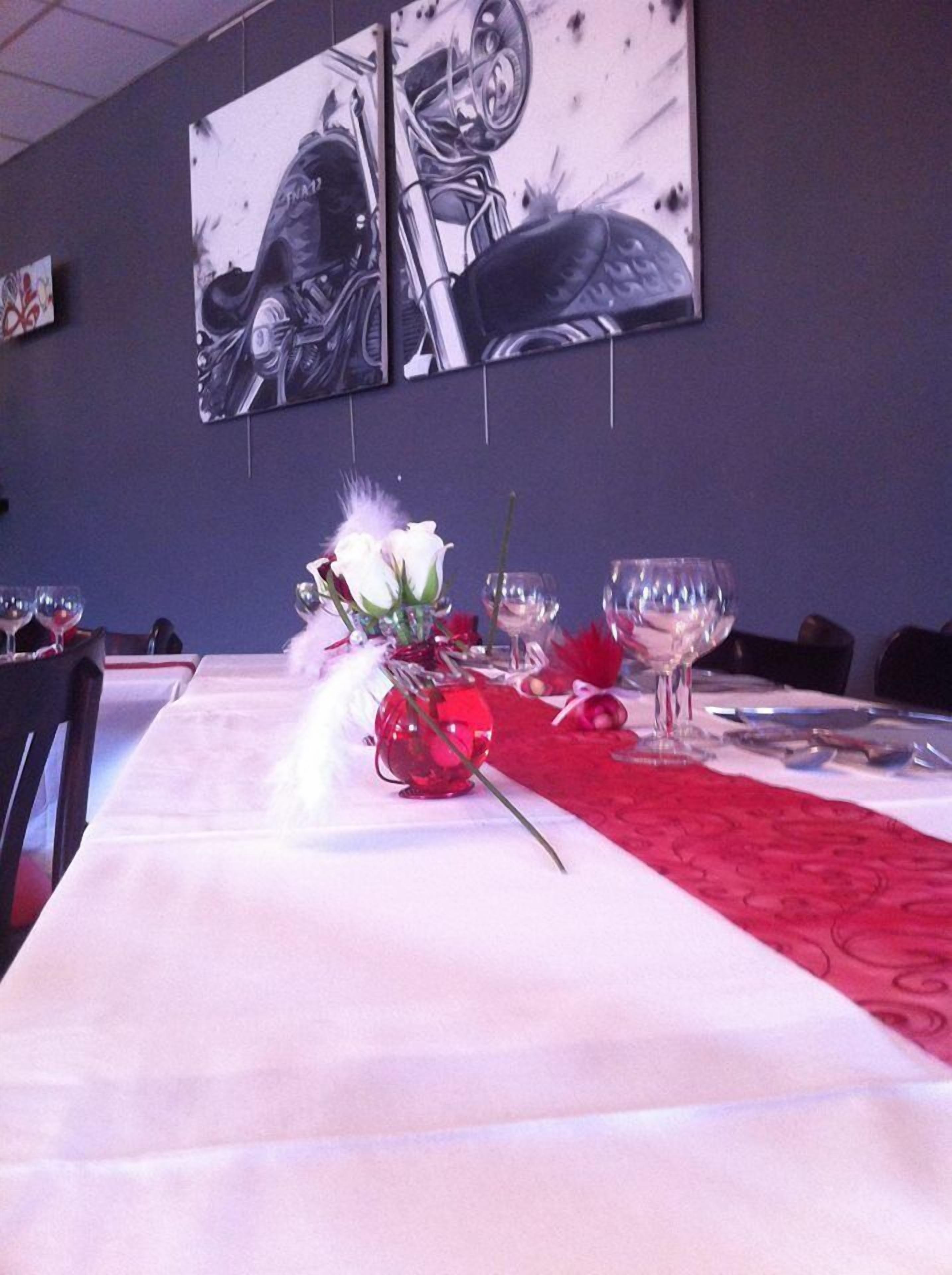 Una mesa de comedor con mantel individual rojo, un florero con flores blancas y copas de vino.