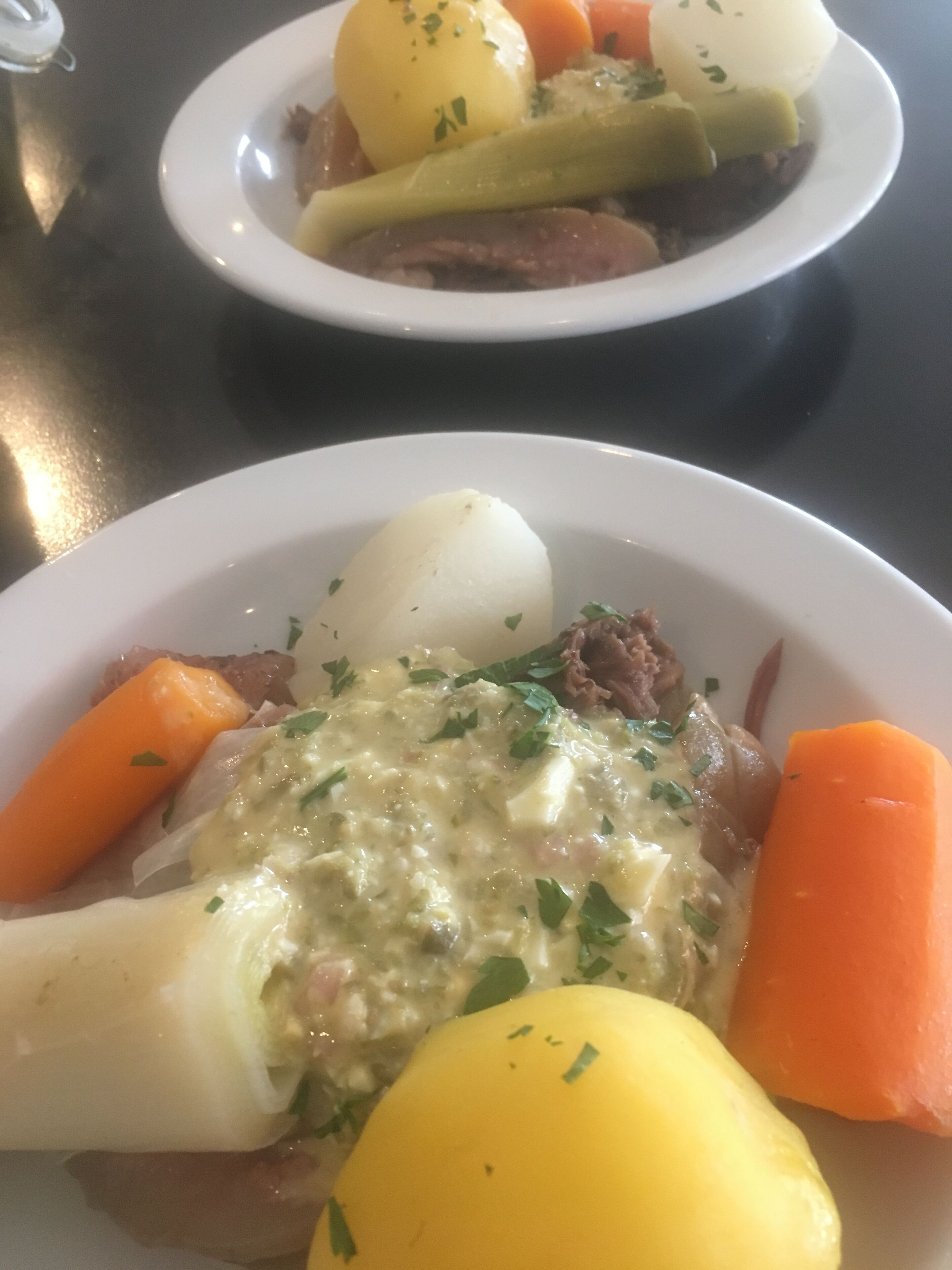 Two white plates with food, including potatoes, carrots, and a yellow item, on a table.