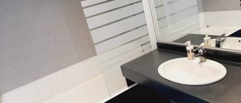 Un baño moderno con un lavamanos blanco, encimera oscura y un espejo grande.