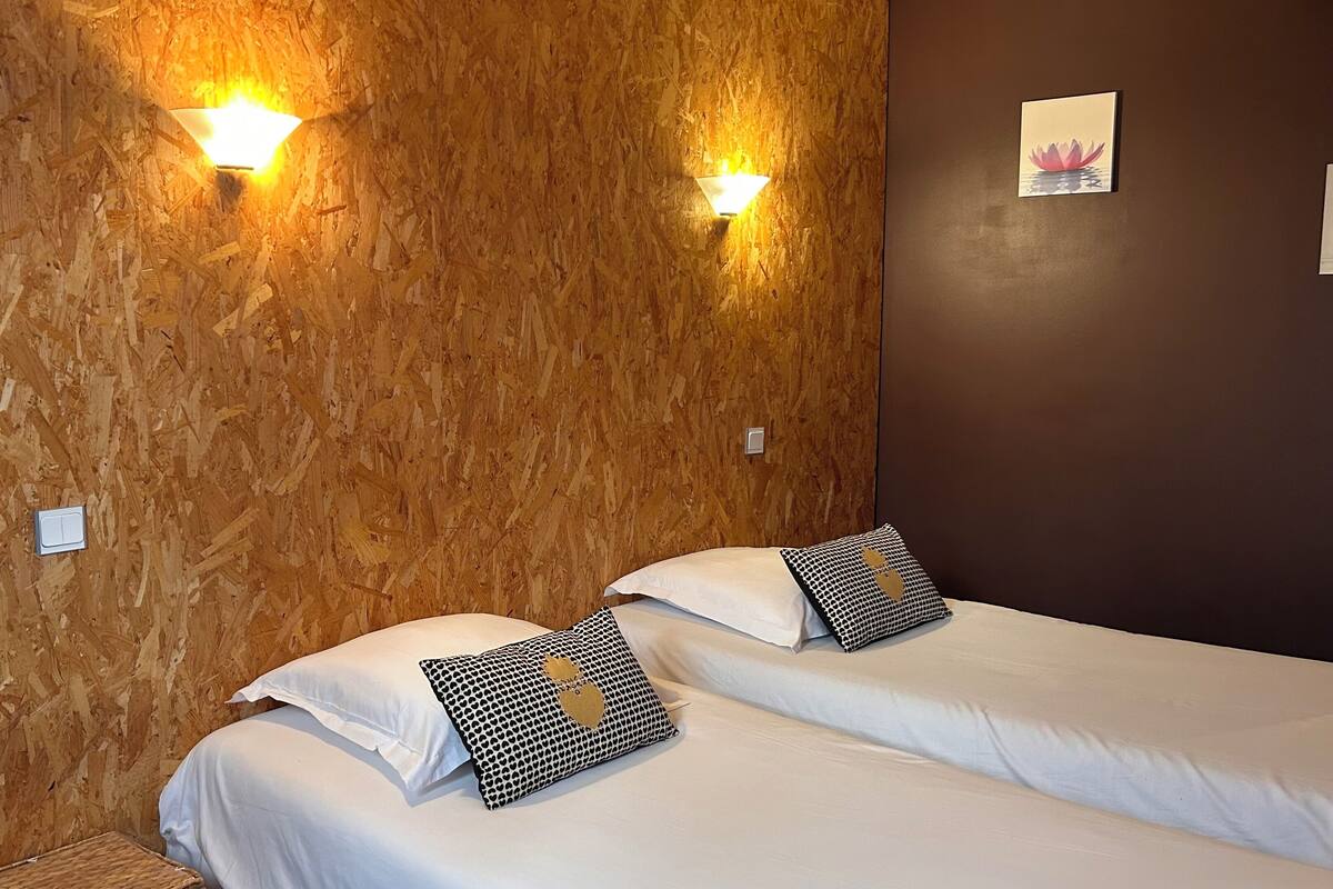 A room with two beds, wooden wall paneling, wall-mounted lights, and a framed picture on the wall.