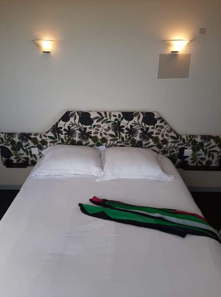 Un lit avec une tête de lit à motifs floraux, deux oreillers et une serviette verte et rouge posée sur le lit.