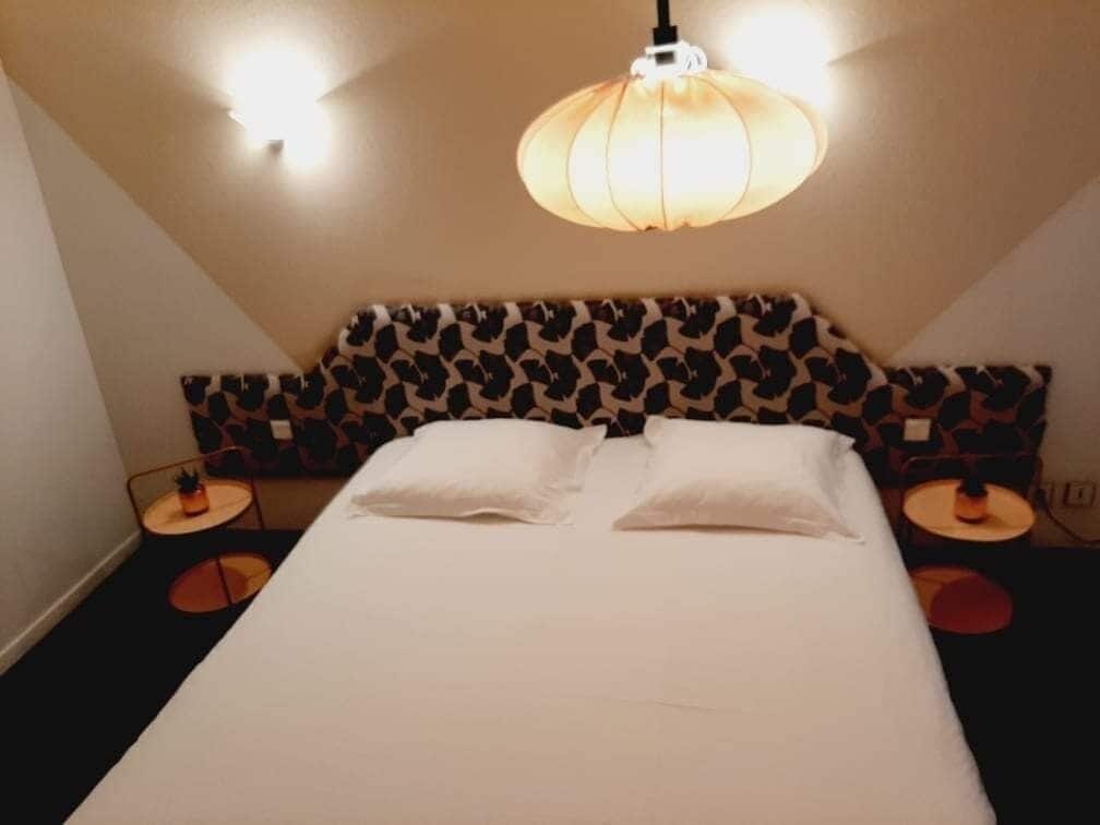 Habitación de hotel con cama, dos mesitas de noche, cabecera estampada y lámpara colgante.