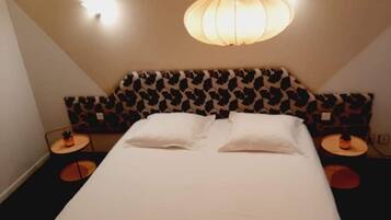 Habitación de hotel con cama, dos mesitas de noche, cabecera estampada y lámpara colgante.