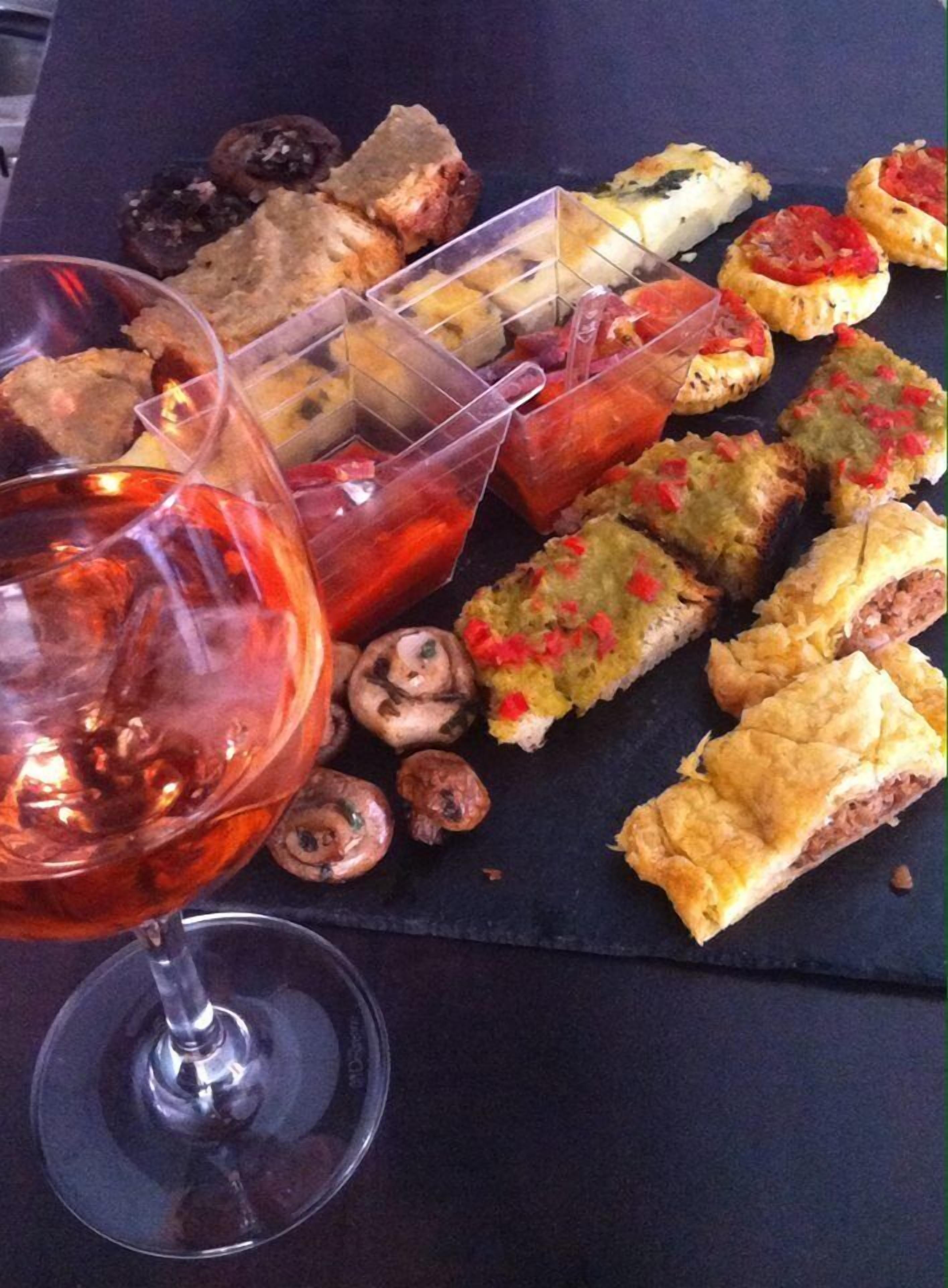 A variety of appetizers and a glass of red wine on a dark slate table.