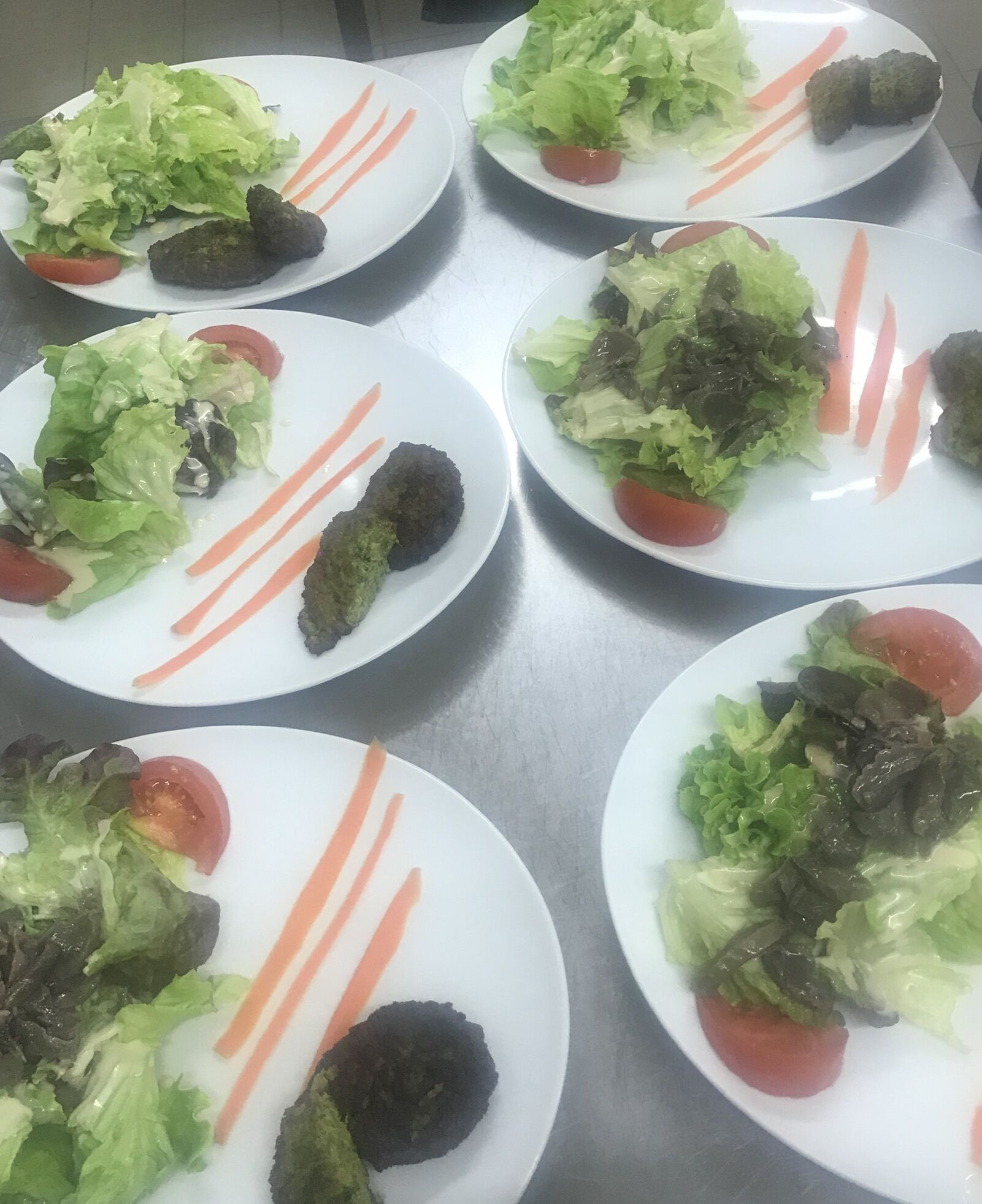 Une table où sont disposées des assiettes remplies de nourriture, notamment des salades et des boulettes de viande, le tout présenté de manière soignée.