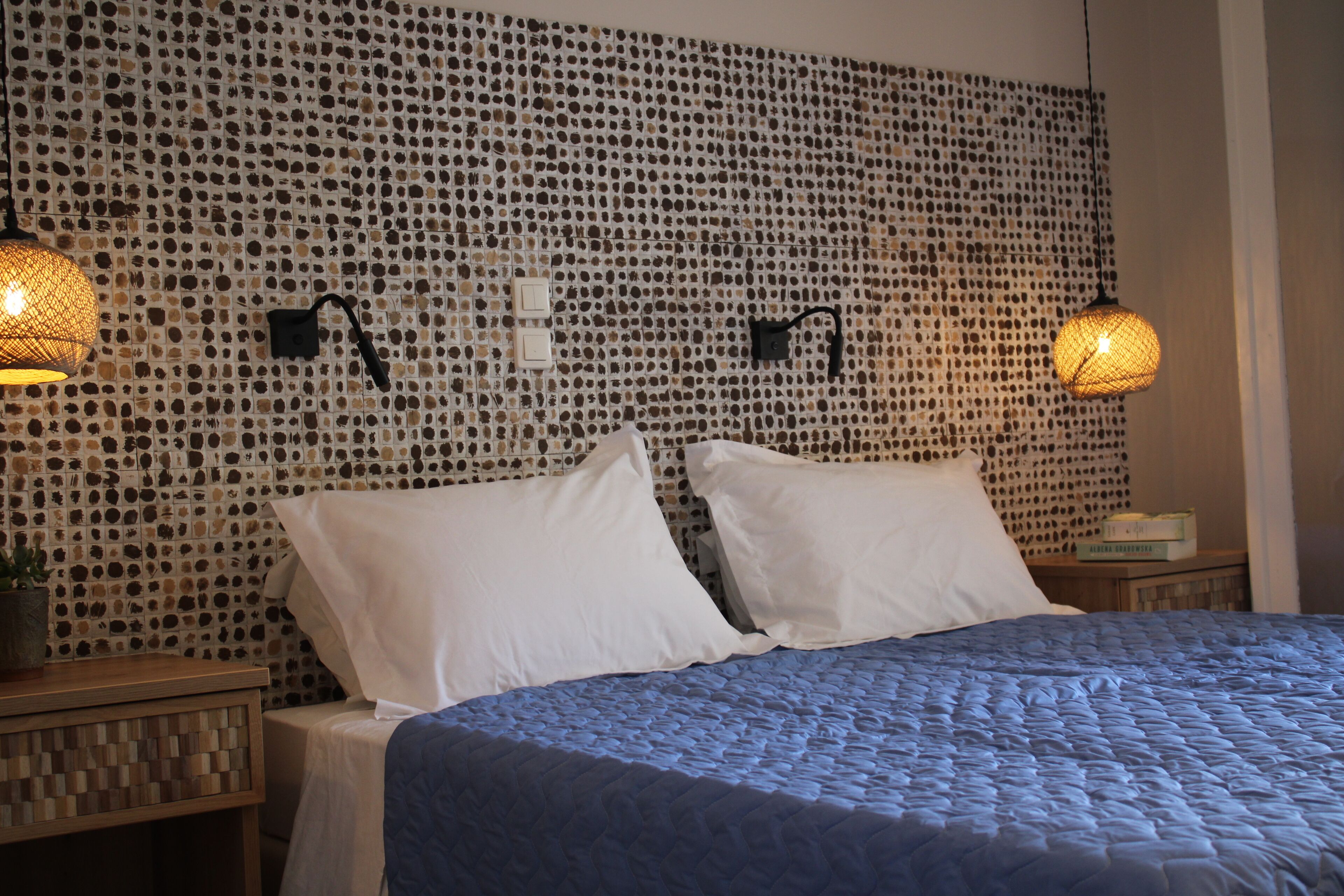 Een net opgemaakt bed met een blauwe quilt, twee witte kussens en een muur met een mozaïekpatroon.