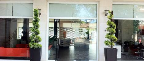 A building entrance with a glass door, two potted plants, and a stone-tiled floor.