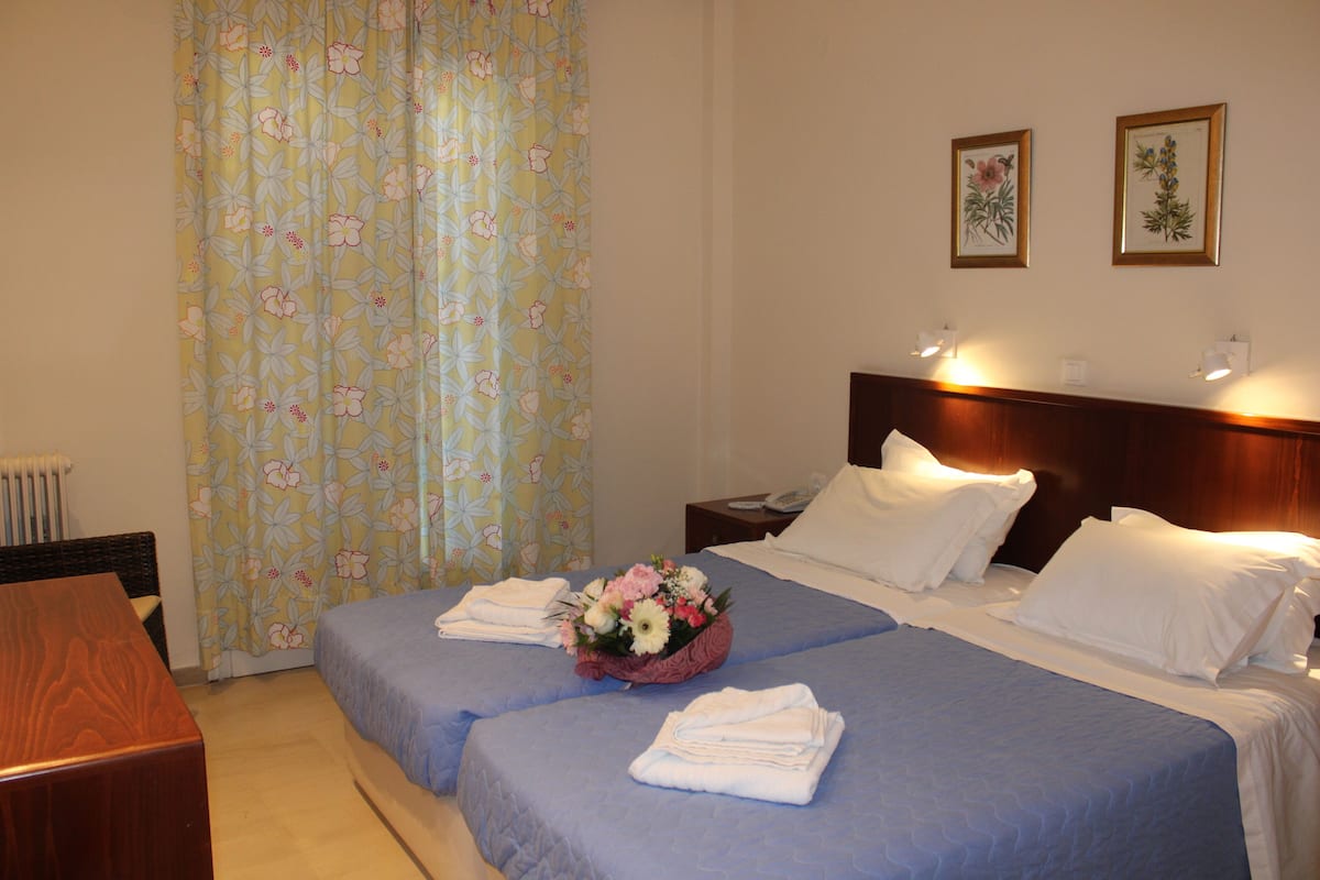 A hotel room with two beds, a wooden desk, and a window with floral curtains.