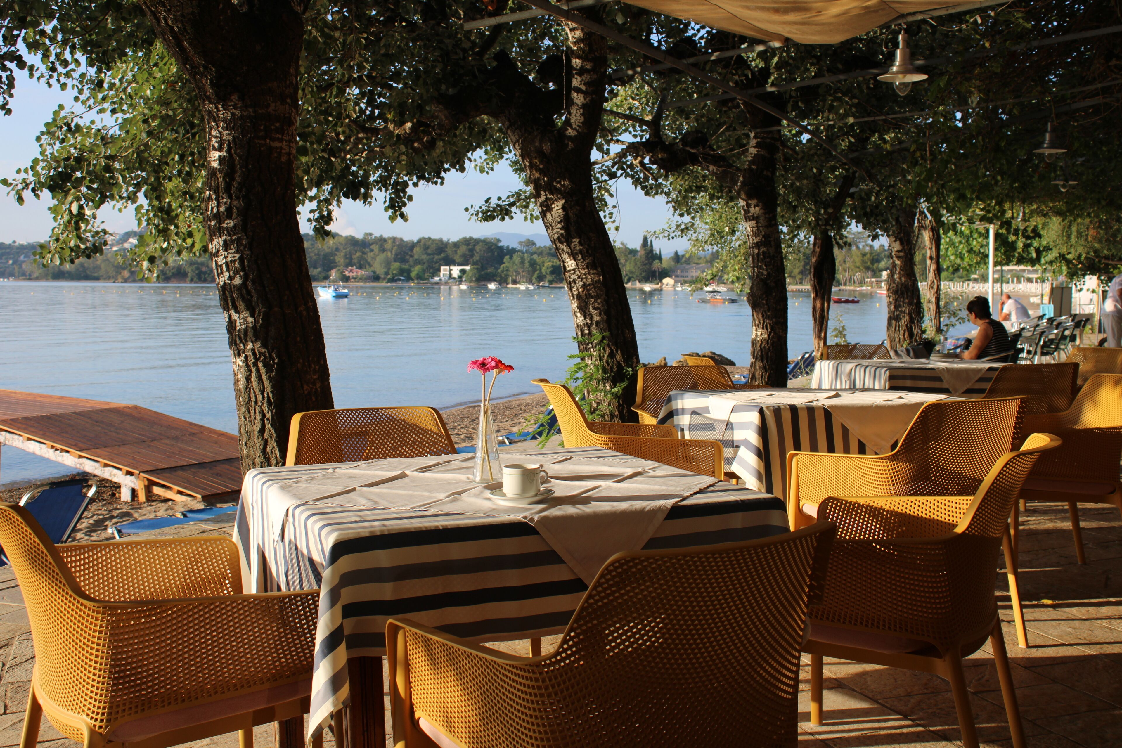 An outdoor dining area with tables and chairs, overlooking a body of water.
